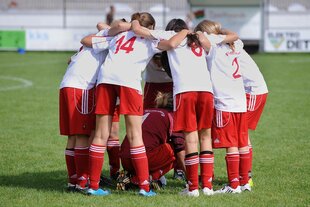 Jugendliche Fußballerinnen die im Kreis stehen und die Torhüterin in die Mitte nehmen