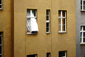 Aus einem Fenster in einem Haus weht eine weiße Gardine