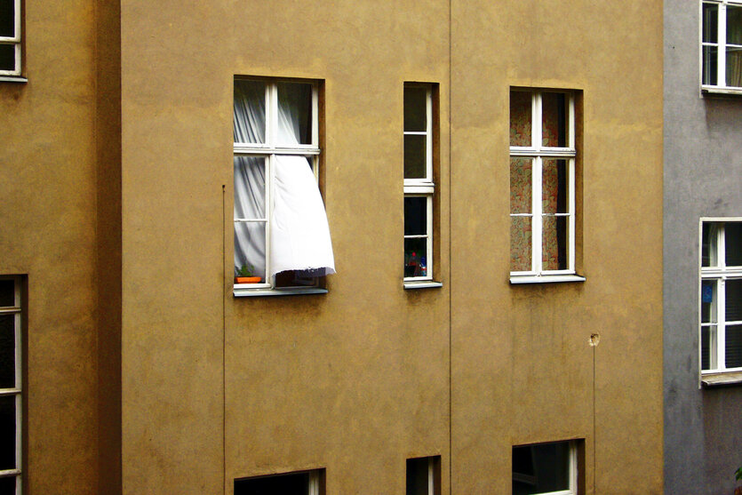 Aus einem Fenster in einem Haus weht eine weiße Gardine