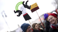 Protestaktion, Demonstrierende halten ein Schild hoch, es zeigt den Berliner Bären der von einer Hand gequetscht wird und das Wort unkürzbar in grün steht zwischen seinen Pfoten