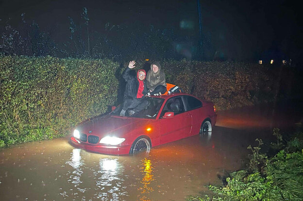 Ein Paar sitzt auf einem Auto auf dem Dach, außerherum Wasser.