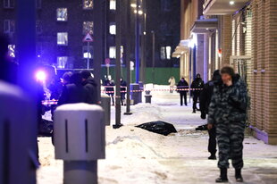 Polizei und Armee auf der verschneiten Strasse, im Hintergrund Absperrbänder, es ist Nacht und die Leichen sind mit schwarzen Säcken bedeckt