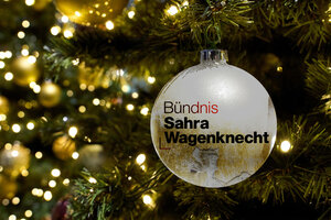 Eine weiße Christbaumkugel mit Aufschrift Sahra Wagenkneckt vor Tannengrün mit Lichterkette