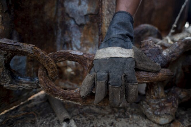 Eine Hand im Arbeitshandschuh und eine verrostete Ankerkette