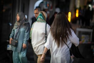 Eine Frau läuft in Teheran mit offenen Haaren am Abend eine Straße entlang.