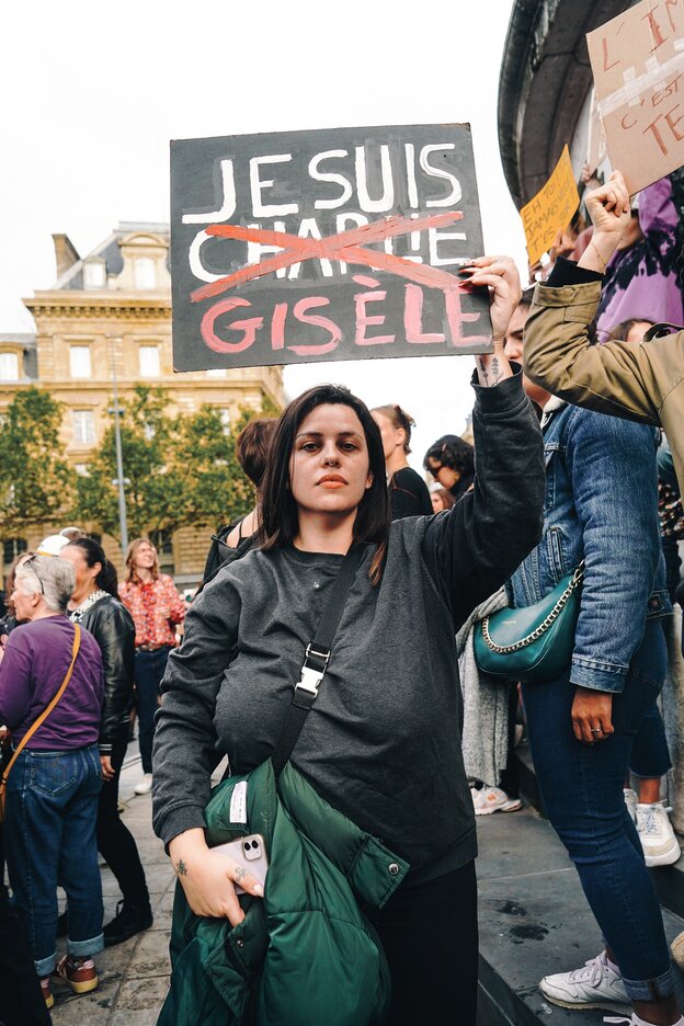 Eine Frau hält ein Schild in die Höhe, darauf ist zu lesen 