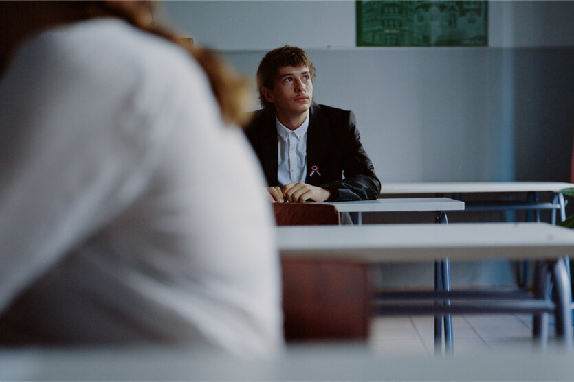 ein junger Mann sitzt auf einer Schulbank und schaut zum Fenster hinaus