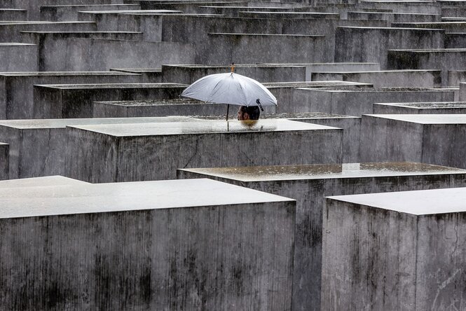 Ein Mensch mit einem Regenschirm zwischen den Stehlen des zentralen Holocaus-Mahnmals in berlin