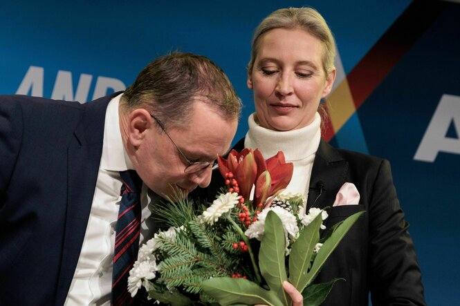 Tino Chrupalla und Alice Weidel schauen auf einen Blumenstrauß