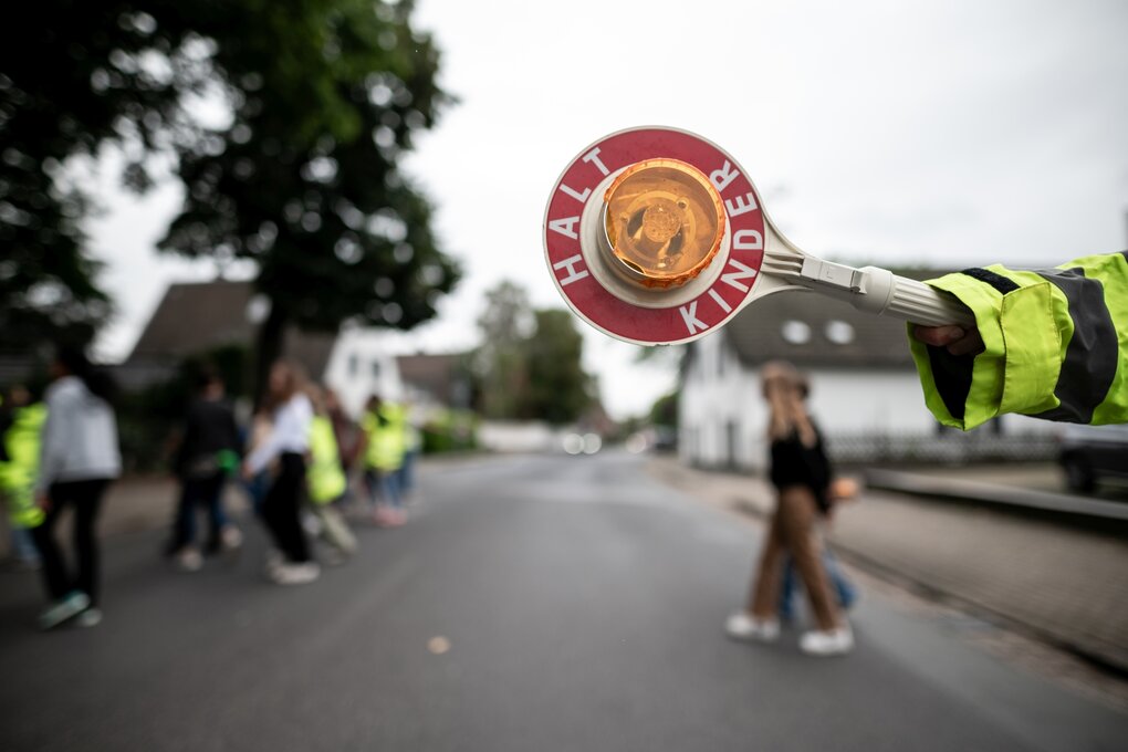 Die Kell eines Schülerlotse, im Hintergrund (unscharf) sieht man Kinder, die gerade eine Straße überqueren