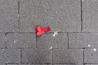 Ein roter Luftballon in Herzform liegt auf dem Straßenpflaster, er ist nicht aufgeblasen