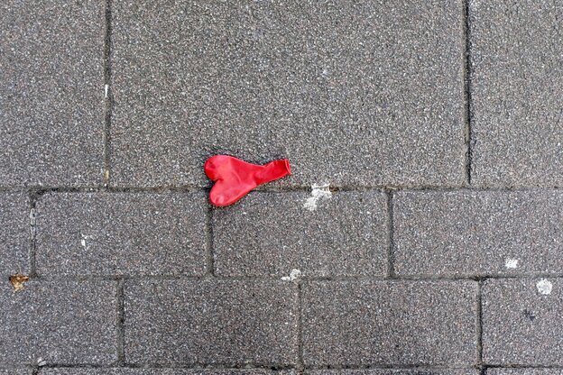 Ein roter Luftballon in Herzform liegt auf dem Straßenpflaster, er ist nicht aufgeblasen