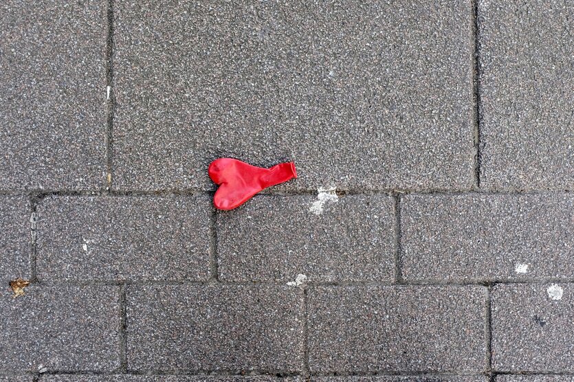 Ein roter Luftballon in Herzform liegt auf dem Straßenpflaster, er ist nicht aufgeblasen