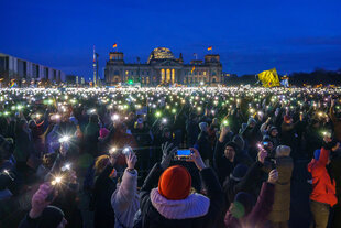 Menschen stehen vor dem Deutschen Bundestag in Berlin und leuchten mit ihren Handys