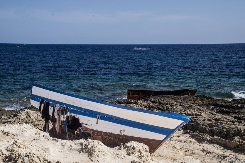 Das Wrack eine blau-weiß gestrichenen Holzboots liegt an einem Strand