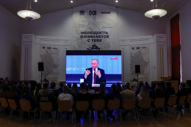 Wladimir Putin bei einer Pressekonferenz, vor der Leinwand mehrere Reihen von Zuhörer*innen