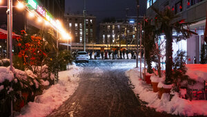 Verschneite Straße bei Nacht in Zürich. Im Hintergrund ist eine Menschenschlange zu erkennen.