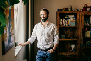 Ein Mann steht mit Jeans und Hemd in einem Raum am Fenster