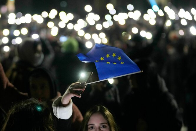 Eine Person mit einem blauen Fähnchen der EU steht in einer Menschenmenge, die Lampen vieler Smartphones leuchten im Dunkeln