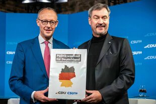 Friedrich März und Markus Söder halten das Wahlprogramm in den Händen und blicken in die Kamera