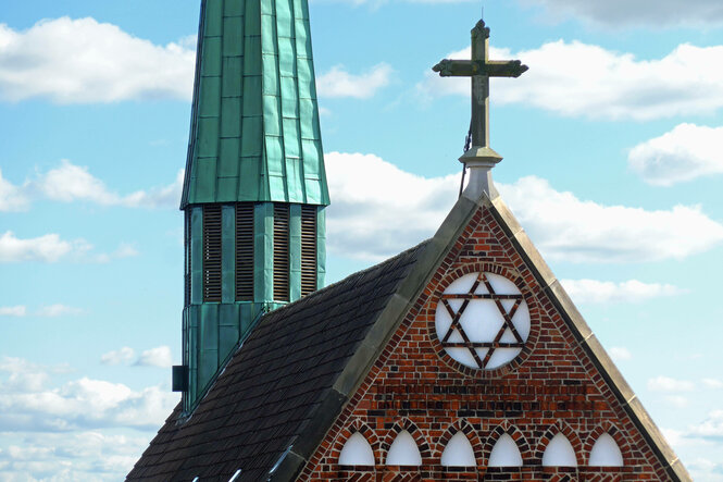 Backsteingiebel einer Kiche mit Davidstern, im Hintergrund ein Turm mit grüner Kupfereindeckung