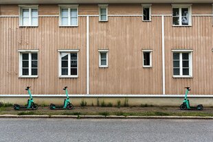 Drei E-Scooter parken vor einem Wohnhaus mit Holzfassade in der Nähe von Jakobstad