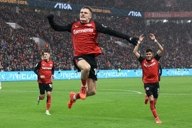 Florian Wirtz springt in der Mitte jubelnd in die Luft. Links und rechts jubelt jeweils ein Mitspieler