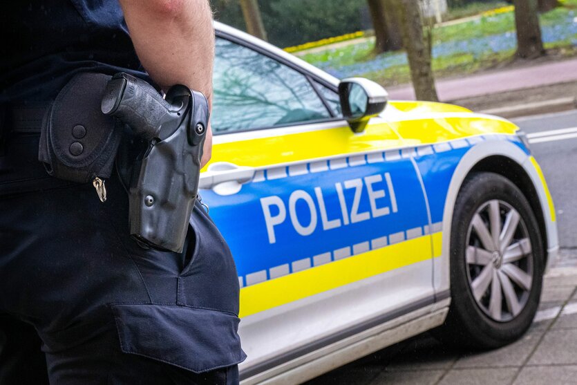 Zu sehen ist ein Polizeiauto und die Hose eines Polizisten mit Waffe