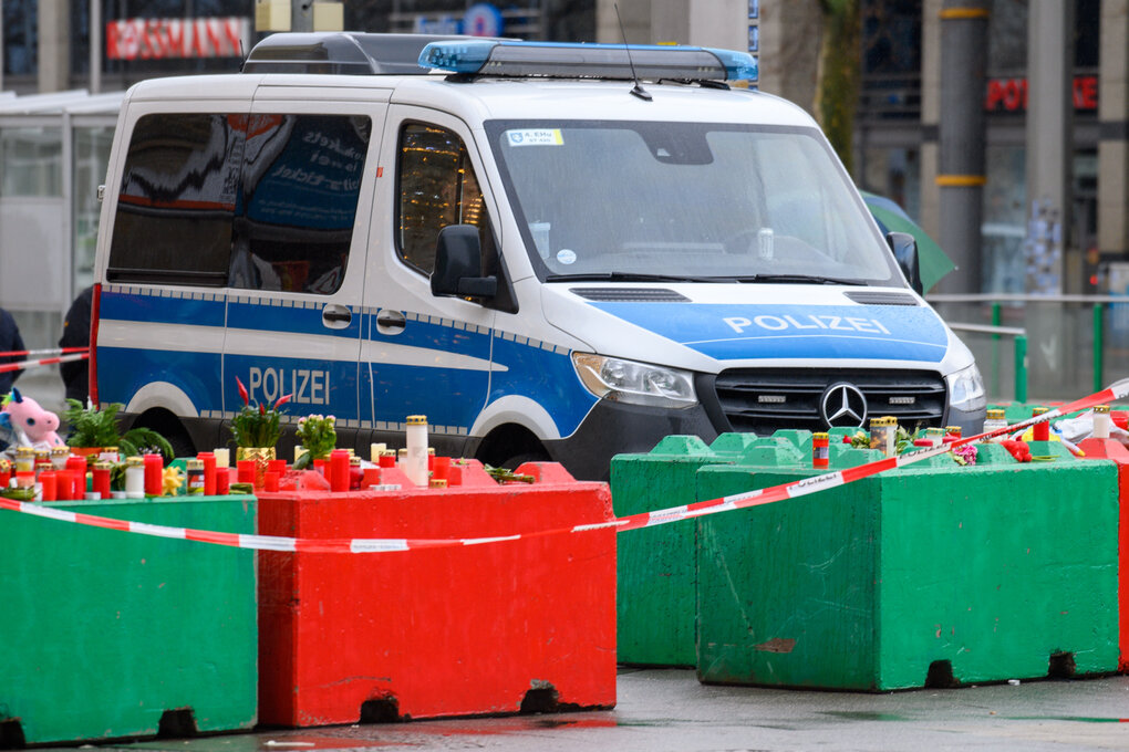 Ein Polizeiwagen steht hinter der Absperrung des Magedeburger Weihnachtsmarktes, auf den bunten Absperrungskästen haben Menschen Blumen und Kerzen niedergelegt.