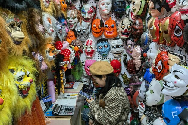 Eine Frau sitzt mit Rechenmaschinen in einem Laden mit Helloween- und Gruselmasken
