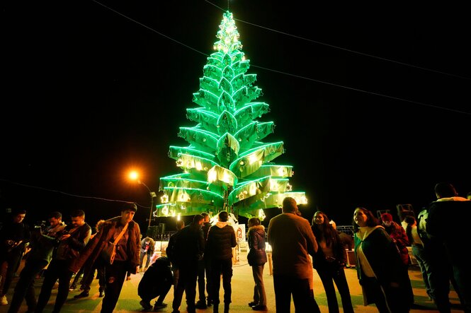 Ein hellerleuchteter Weihnachtsbaum im Freien. Es ist dunkel, einige Menschen stehen davor.