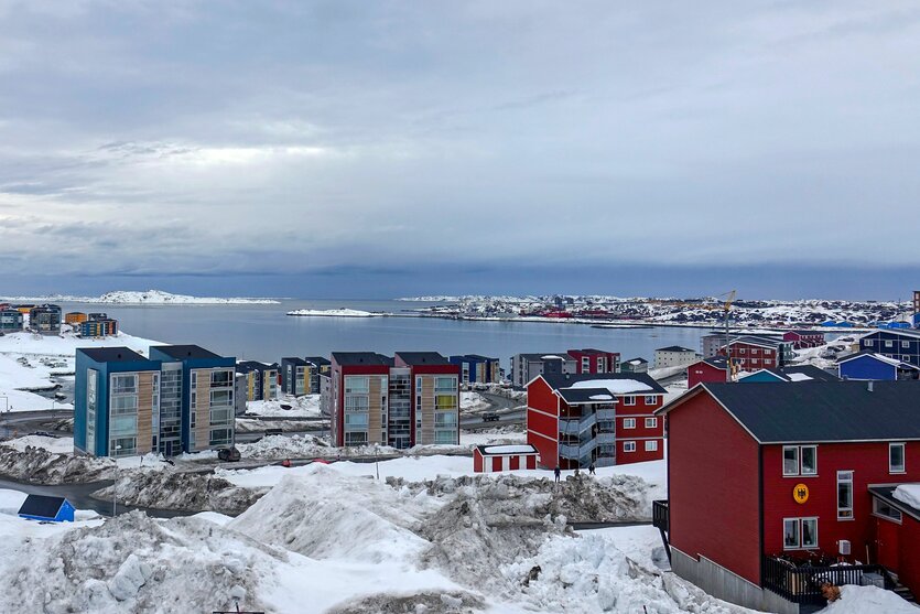 Häuser umgeben von Schnee, im Hintergrund eine von Fjorden gesäumte Küste