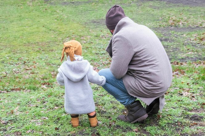 Vater hockt mit Kleinkind auf einer Wiese