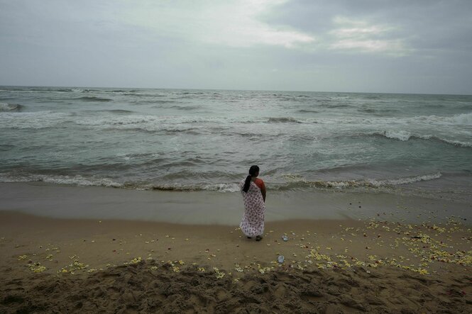 Eine Person steht am Strand und blickt auf das Meer, auf dem Boden liegen bunte Blumen verstreut