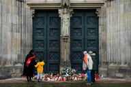 Vier menschen stehen vor dem Eingang zu einer Kirche und legen Blumen nieder