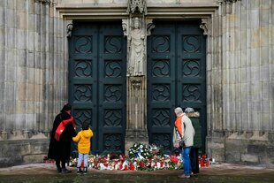 Vier menschen stehen vor dem Eingang zu einer Kirche und legen Blumen nieder