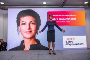 Sahra Wagenknecht steht vor einem Plakat mit ihrem Konterfei