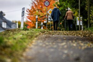 Zwei ältere Menschen sind auf einem mit Laub bedeckten Weg mit Nordic-Walking-Stöcken unterwegs, sie sind nur von hinten zu sehen