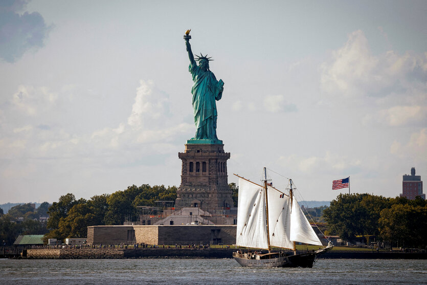 Die Freiheitsstatue von New York aus der Ferne, davor fährt ein Segelboot