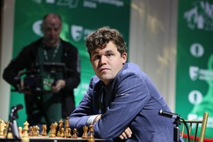 Carlsen sitzt am Schachbrett und schaut in die Kamera