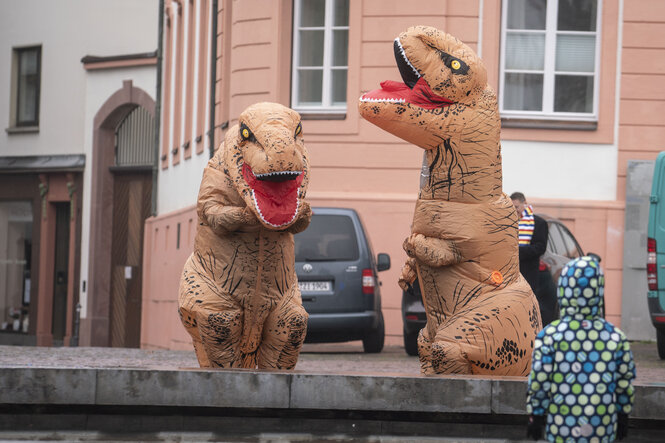 Zwei Dinosaurierfiguren vor einem Haus, beobachtet von einem Kind