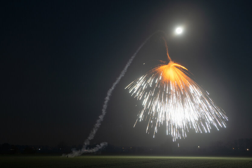 Eine Feuerwerksrakete explosiert über einer weiten Wiese.