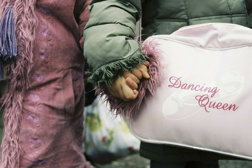 Zwei Kinder halten Händchen, eins trägt eine Tasche auf der "Dancing Queen" steht