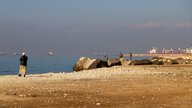 An einem Strand sieht man mehrere Männer iun Uniformen, einer zielt mit seinem Gewehr auf das Meer