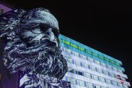 Karl-Marx-Statue vor einem Hochhaus in experimenteller Beleuchtung