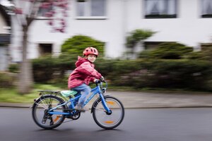 Kind fährt mit Rad auf der Straße vor einem Haus vorbei