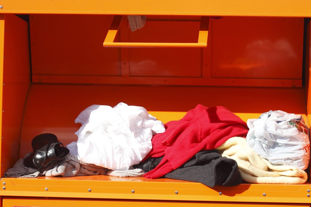 Klappe eines orangen Altkleidercontainers beladen mit Kleidung und Schuh