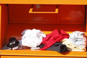 Klappe eines orangen Altkleidercontainers beladen mit Kleidung und Schuh