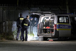 im Dunkeln stehen Polizisten neben einem Polizefahrzeug an einem Zaun