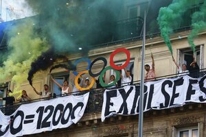 Protestierende stehen mit Pyrofackeln auf dem Balkon und halten selbst gebastelte olympische Ringe hoch